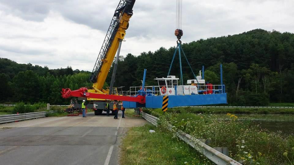 a crane is lowering a dredge into a lake